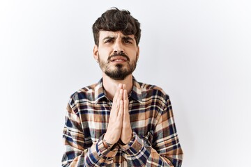 Hispanic man with beard standing over isolated background begging and praying with hands together with hope expression on face very emotional and worried. begging.
