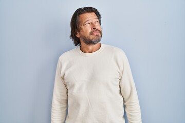 Handsome middle age man wearing casual sweater over blue background looking away to side with smile on face, natural expression. laughing confident.