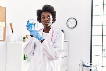 Young african american woman wearing doctor uniform holding syringe at clinic