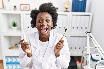 African dentist woman holding electric toothbrush and normal toothbrush celebrating crazy and...