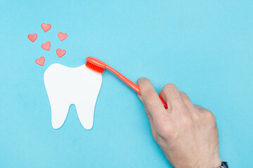 Man cleans a model of a tooth with a toothbrush. Concept against caries. Flat lay. Top view. Dental care. Oral hygiene. Blue background. Hearts.