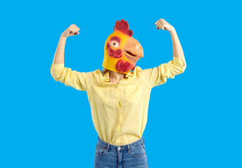 Woman in funny chicken disguise pretends to be super strong. Portrait of confident young girl wearing strange weird ridiculous absurd bizarre Hallowen mask flexing her arms isolated on blue background - Powered by Adobe