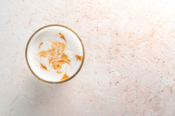 A glass of sweet macchiato or latte with a foam pattern on a white stone table. Coffee mug in minimalist style for the menu, top view