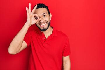 Hispanic man with beard wearing casual red t shirt doing ok gesture with hand smiling, eye looking...
