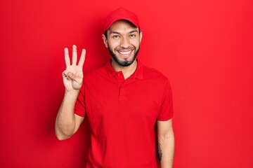 Naklejka premium Hispanic man with beard wearing delivery uniform and cap showing and pointing up with fingers number three while smiling confident and happy.