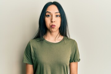 Young hispanic girl wearing casual t shirt puffing cheeks with funny face. mouth inflated with air,...