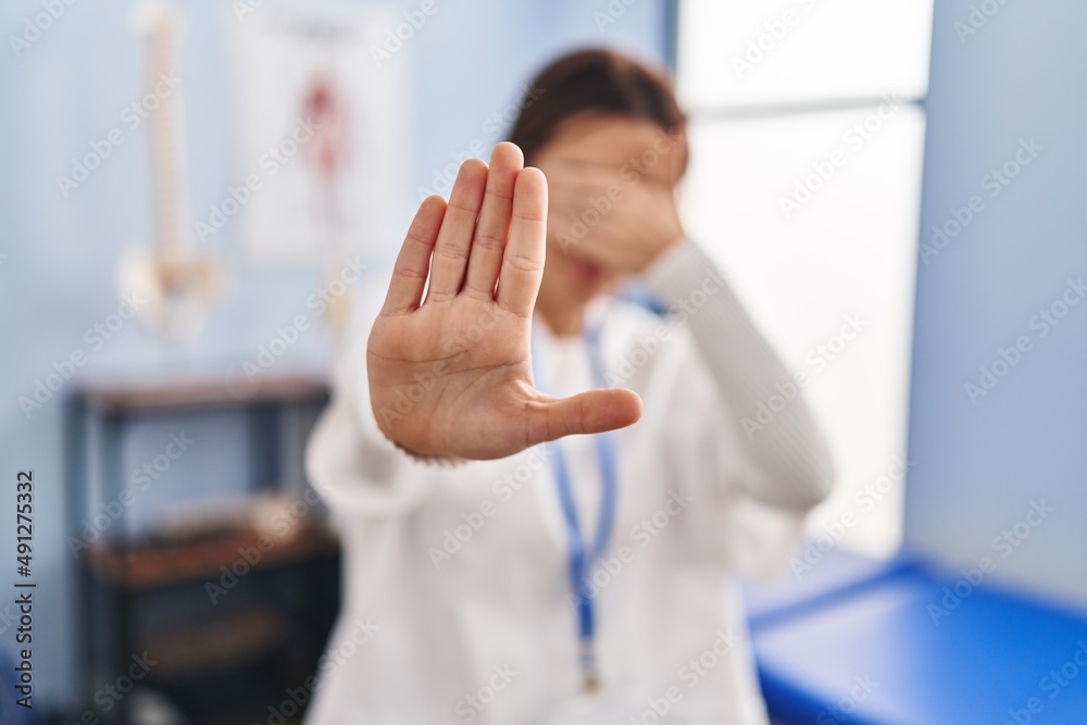 Canvas Prints young brunette woman working at pain recovery clinic covering eyes with hands and doing stop gesture