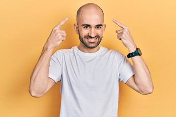 Fototapeta premium Young bald man wearing casual white t shirt smiling pointing to head with both hands finger, great idea or thought, good memory