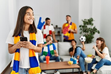 Group of young friends watching and supporting soccer match. Woman smiling happy using smartphone at home.