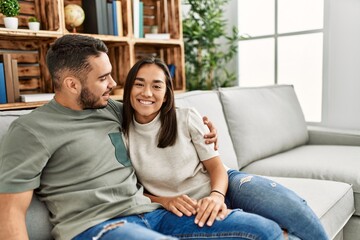 Fototapeta premium Young latin couple sitting on the sofa hugging at home.