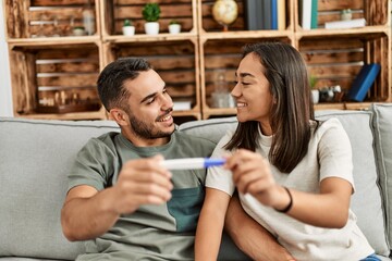 Young latin couple smiling happy looking pregnant test result at home.