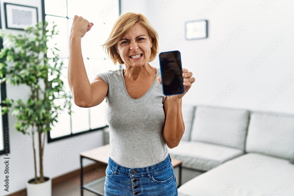 Sticker middle age blonde woman working holding smartphone showing screen annoyed and frustrated shouting wi