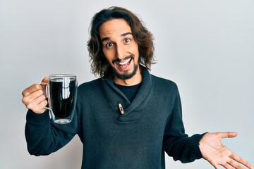 Young hispanic man drinking a cup of coffee celebrating achievement with happy smile and winner expression with raised hand