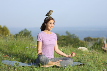 Happy woman doing yoga distracted with a bird on head