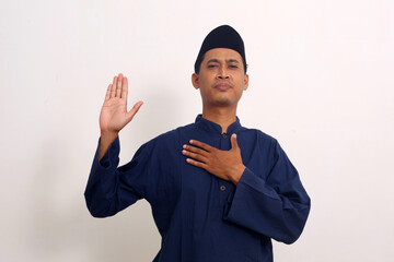 Asian muslim man standing while making promise gesture. Isolated on white background