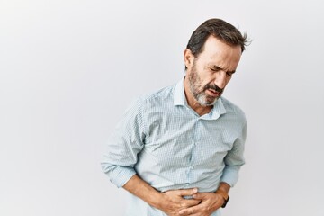 Middle age hispanic man with beard standing over isolated background with hand on stomach because indigestion, painful illness feeling unwell. ache concept.