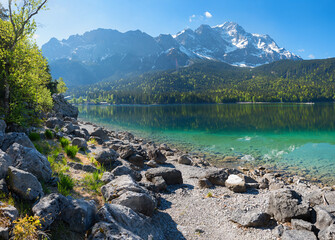 rocky bathing beach at lake shore Eibsee, view to Zugspitze mountain, upper bavaria in spring