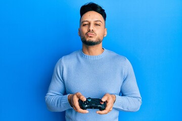 Young arab man playing video game holding controller looking at the camera blowing a kiss being lovely and sexy. love expression.