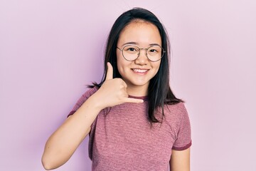 Fototapeta premium Young chinese girl wearing casual clothes and glasses smiling doing phone gesture with hand and fingers like talking on the telephone. communicating concepts.