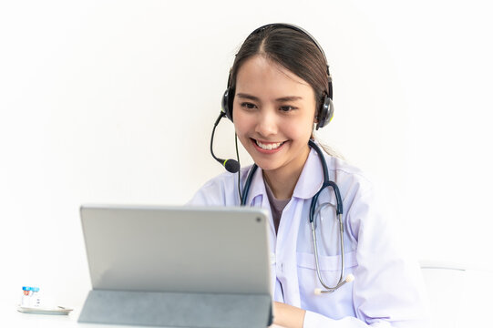 Portrait photo of young beautiful Asian doctor video remote conference call online with patient for social distancing due to covid-19 pandemic. Technology, health care new normal online telehealth.