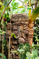 Stone carved totem with  human face among tropical plants
