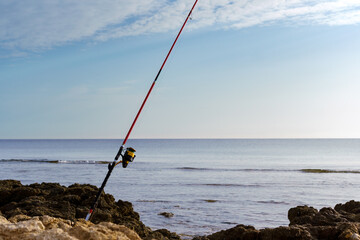 A fisherman has left his fishing rod in place on the rocks by the sea.