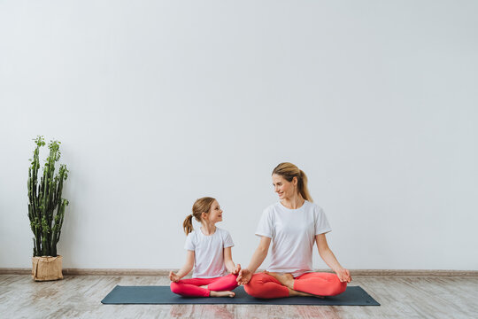 mother and daughter do yoga in a bright room. Paired yoga with a child. girls sit in the butterfly pose and smile Happiness and harmony. Baddha Konasana.