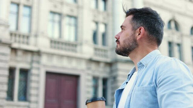 Portrait of stylish handsome caucasian young man walking in the city and drinking coffee to go while relaxing after work