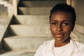 Fototapeta premium Close-up view of an African American woman looking at the camera with a serious expression on her face while posing on the stairs.
