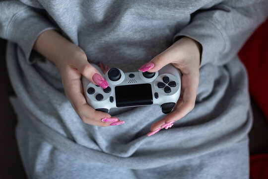 In the hands of a young girl, a joystick with which she plays a video game, a gray sweatshirt on the girl, a pink manicure with ornaments on her long nails, beads, a figurine, stickers, a drawing