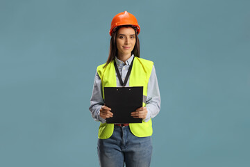 Young female engineer with a safety vest and hardhat holding a clipboard