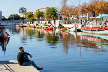 Fototapeta na wymiar Man sitting in the center of Aveiro contemplating the water canal and the boats.