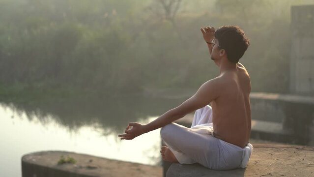 Young indian boy doing yoga early in the morning, boy doing anulom vilom near a river.