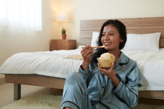 Cheerful young woman eating bowl of delicious icecream and watching new show on tv at home