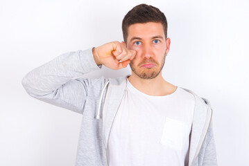Unhappy young caucasian man wearing casual clothes over white background crying while posing at camera whipping tears with hand.