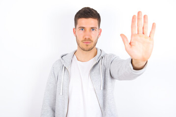Fototapeta premium young caucasian man wearing casual clothes over white background doing stop gesture with palm of the hand. Warning expression with negative and serious gesture on the face.
