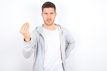 What the hell are you talking about. Shot of frustrated young caucasian man wearing casual clothes over white background gesturing with raised hand doing Italian gesture, frowning, being displeased 