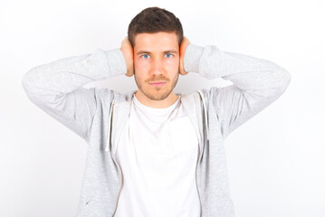 Frustrated young caucasian man wearing casual clothes over white background plugging ears with hands does not wanting to listen hard rock, noise or loud music.