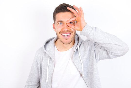 young caucasian man wearing casual clothes over white background with happy face smiling doing ok sign with hand on eye looking through finger.