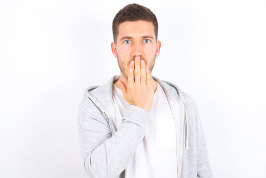 Oh! I think I said it! Close up portrait young caucasian man wearing casual clothes over white background cover open mouth by hand palm, look at camera with big eyes.