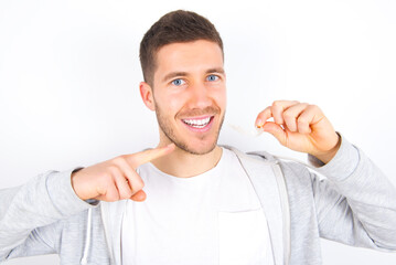 young caucasian man wearing casual clothes over white background  holding an invisible aligner and...