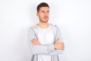 Charming thoughtful young caucasian man wearing casual clothes over white background  stands with arms folded concentrated somewhere with pensive expression thinks what to do