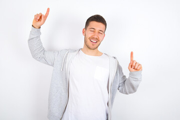 Photo of upbeat young caucasian man wearing casual clothes over white background  has fun and dances carefree wear being in perfect mood makes movements. Spends free time on disco party