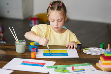 Sad child girl draws a picture of the war in Ukraine. Bright drawing with colors of the State flag...