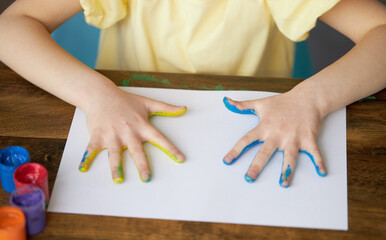 A sad child girl shows her hands painted in the colors of the Ukrainian flag, yellow and blue. Little Ukrainian patriot. Stop the war. Military conflict between Russia, Ukraine and the United States.