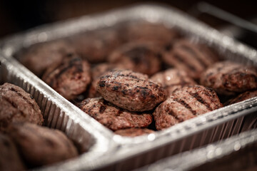Traditional Bulgarian barbecued ground meat called kyufte served as a catering setting placed in aluminum foil pan