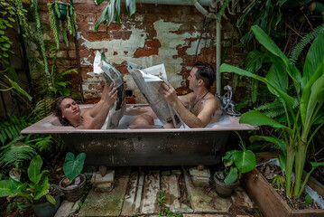 A couple sitting in an outdoor bath ignore each other while they read newspapers. 