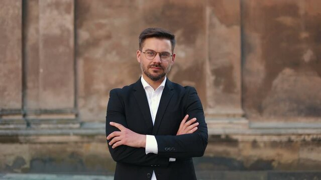 Handsome businessman wearing glasses standing city at the background and smiling broadly at the camera. Close up face of cool trendy bearded man looking at camera