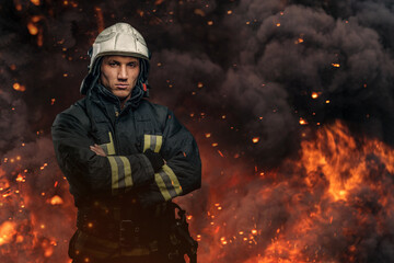 Fireman with crossed arms posing against flame and explosions