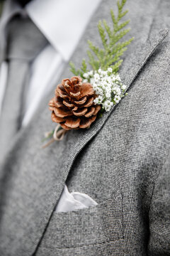 Groom in a grey suit with a pine cone and greenery boutonnière Cropped photo Close up Man in a grey suit with grey tie Groom's accessories Wedding details of the groom